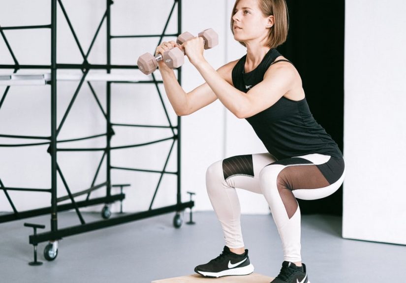 A woman in sportswear performs a squat with dumbbells indoors, embodying strength and healthy living.