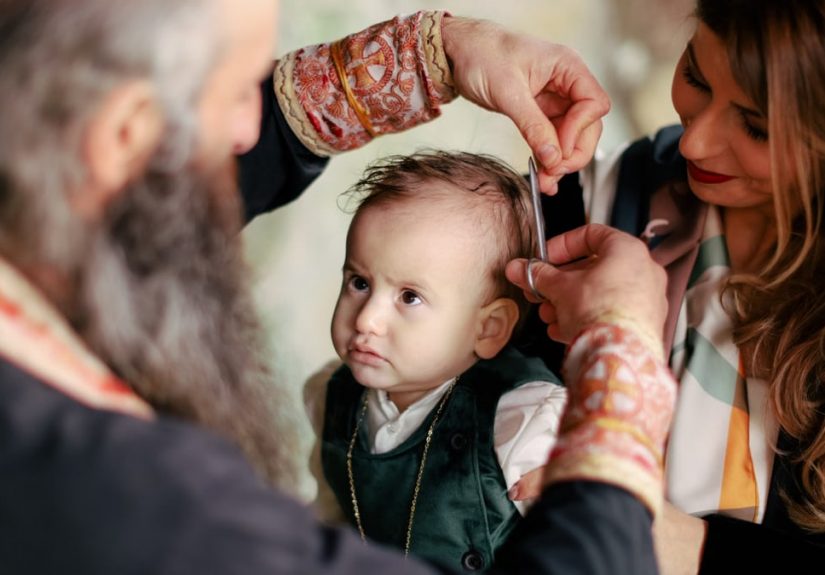 A baby's first haircut performed during a religious ritual with parents and clergy present.