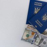 Top view of two Ukrainian passports with US dollar bills on a white surface.