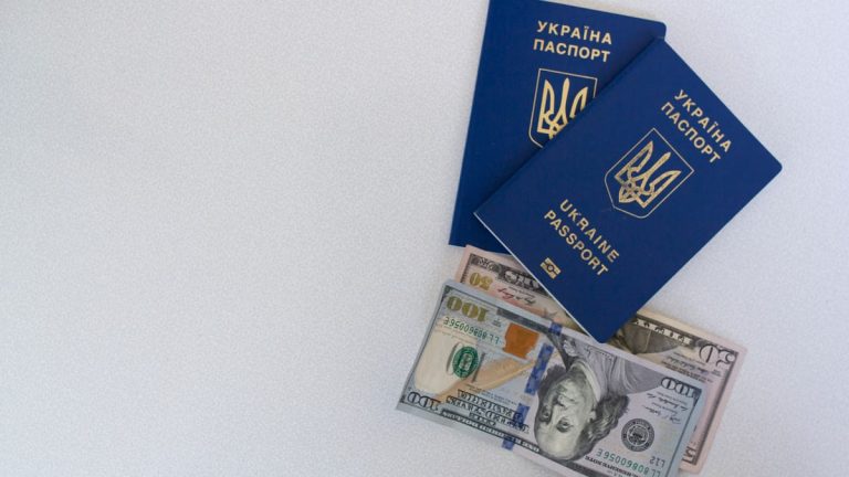 Top view of two Ukrainian passports with US dollar bills on a white surface.