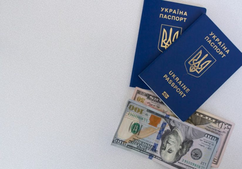 Top view of two Ukrainian passports with US dollar bills on a white surface.