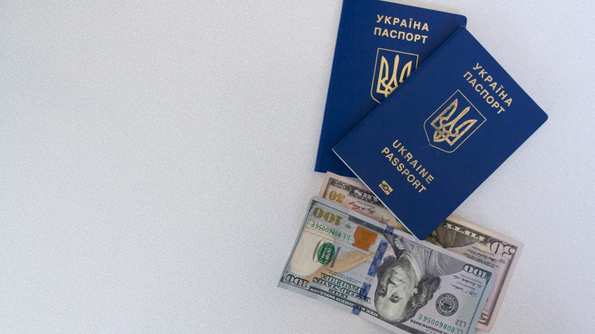 Top view of two Ukrainian passports with US dollar bills on a white surface.